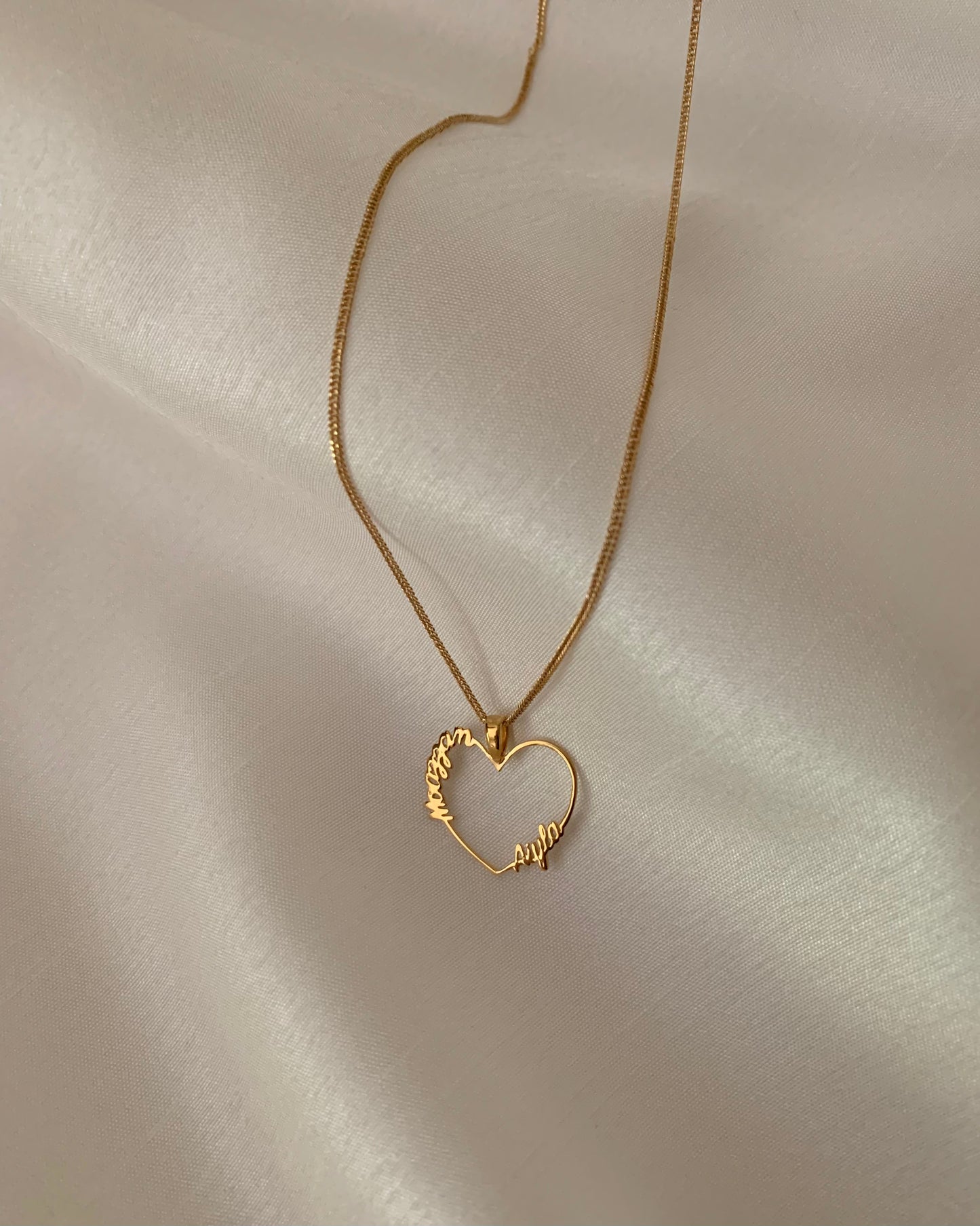 A gold heart-shaped pendant with two names on both sides of it.