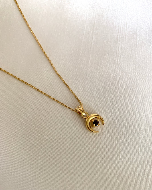 A gold crescent downside moon with a round garnet stone. All set in yellow gold.