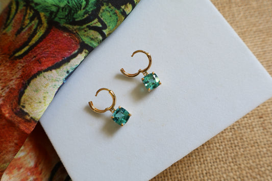 Custom 18K yellow gold huggie hoop earrings featuring cushion-cut ocean-blue gemstones in a dangling drop design, inspired by the beauty of the sea.