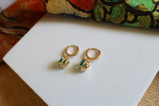Custom 18K yellow gold huggie hoop earrings featuring cushion-cut ocean-blue gemstones in a dangling drop design, inspired by the beauty of the sea.