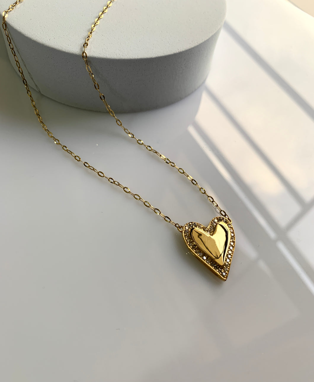 A gold heart pendant with shiny round diamonds around the heart itself. 