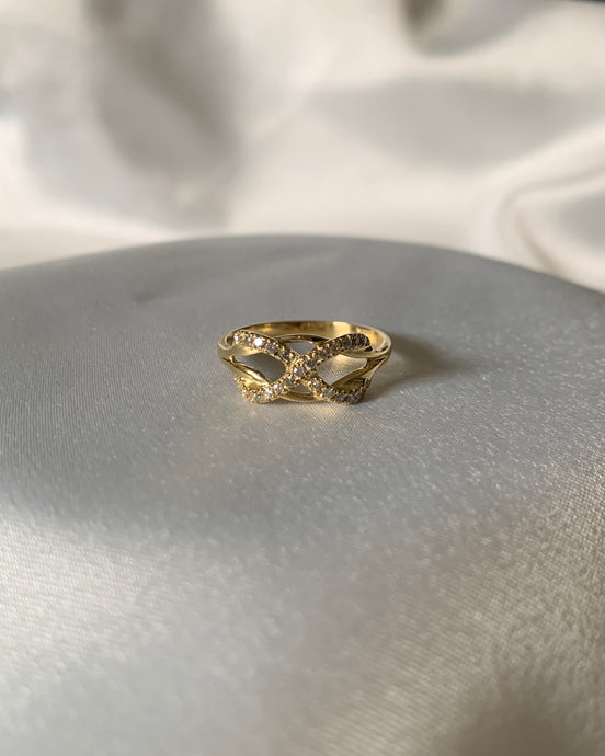 A gold infinity ring with small round shiny diamonds on the infinity symbol itself. Wrapped around a knot.