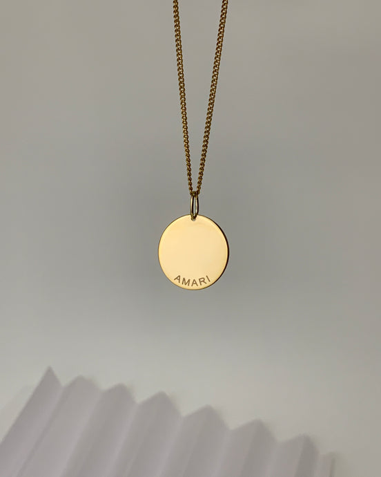 A 14 karat gold customized disc pendant with the name Amari engraved in front. 