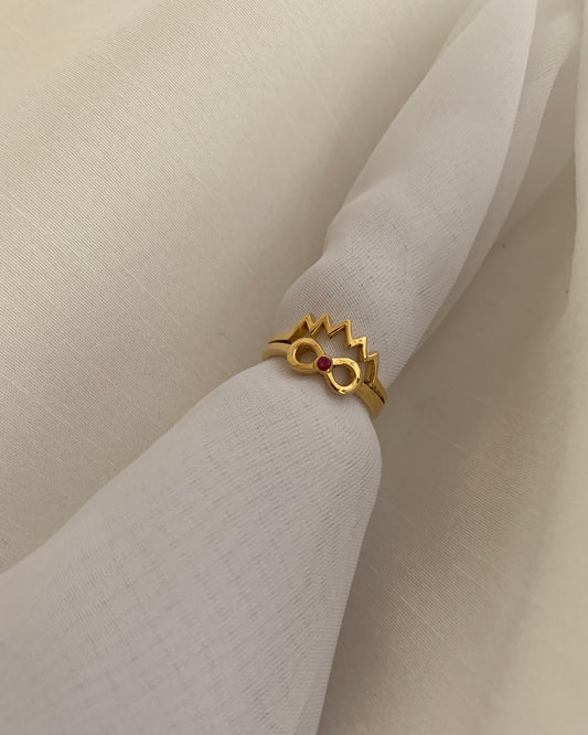 An inifinity sign with a round ruby stone as the center stone and a crown above its. All set on 14k gold.