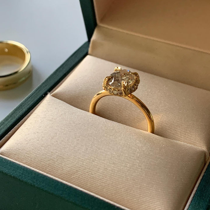 An oval diamond upheld through an under hidden halo set in 18K yellow gold.