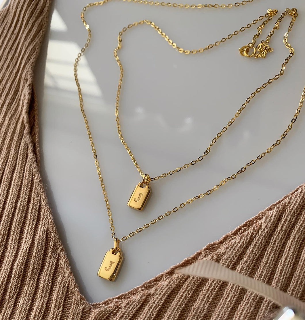 Gold price tag necklace with an engraved initial.