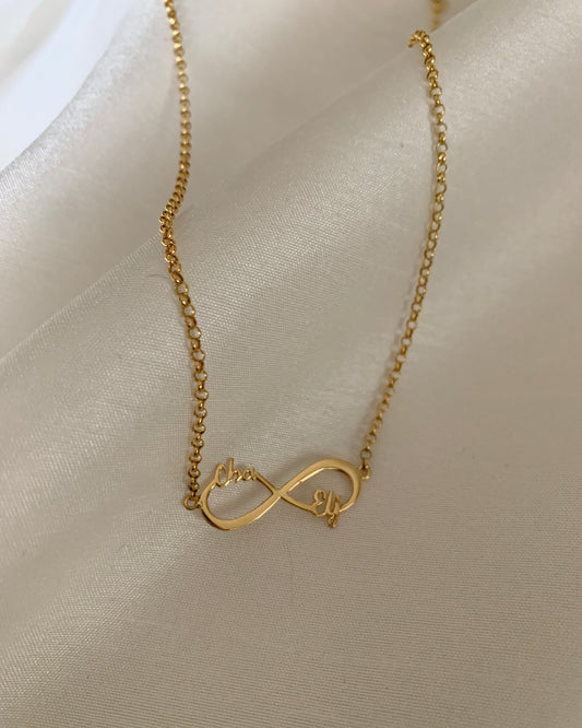 A gold infinity necklace inserted with two cursive names on opposite sides of the pendant. Set in yellow gold.