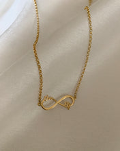 Load image into Gallery viewer, A gold infinity necklace inserted with two cursive names on opposite sides of the pendant. Set in yellow gold.
