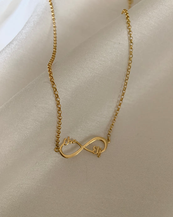 A gold infinity necklace inserted with two cursive names on opposite sides of the pendant. Set in yellow gold.