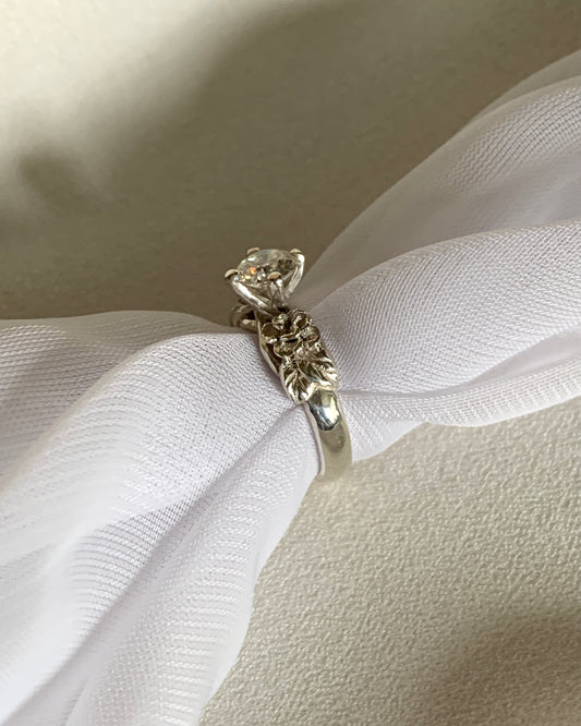 A round solitaire ring with carved roses on the side, set in white gold.