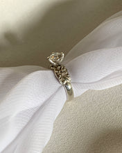Load image into Gallery viewer, A round solitaire ring with carved roses on the side, set in white gold.
