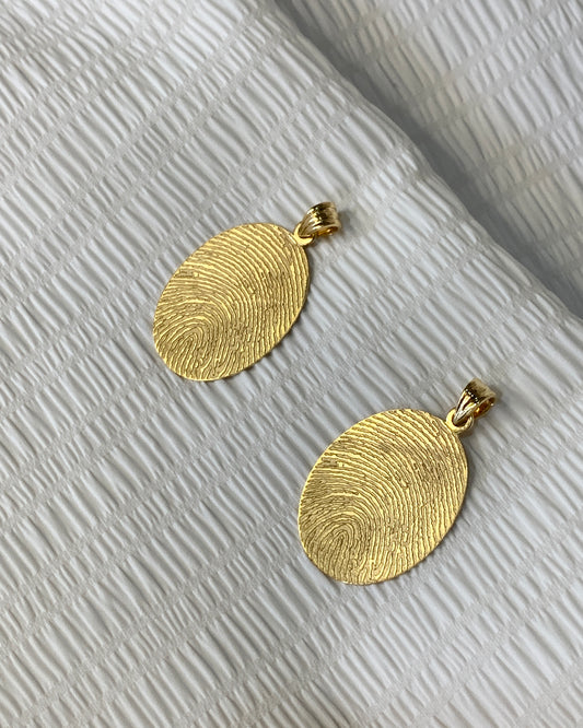 Gold oval fingerprint pendant with engraving of signature at the back.