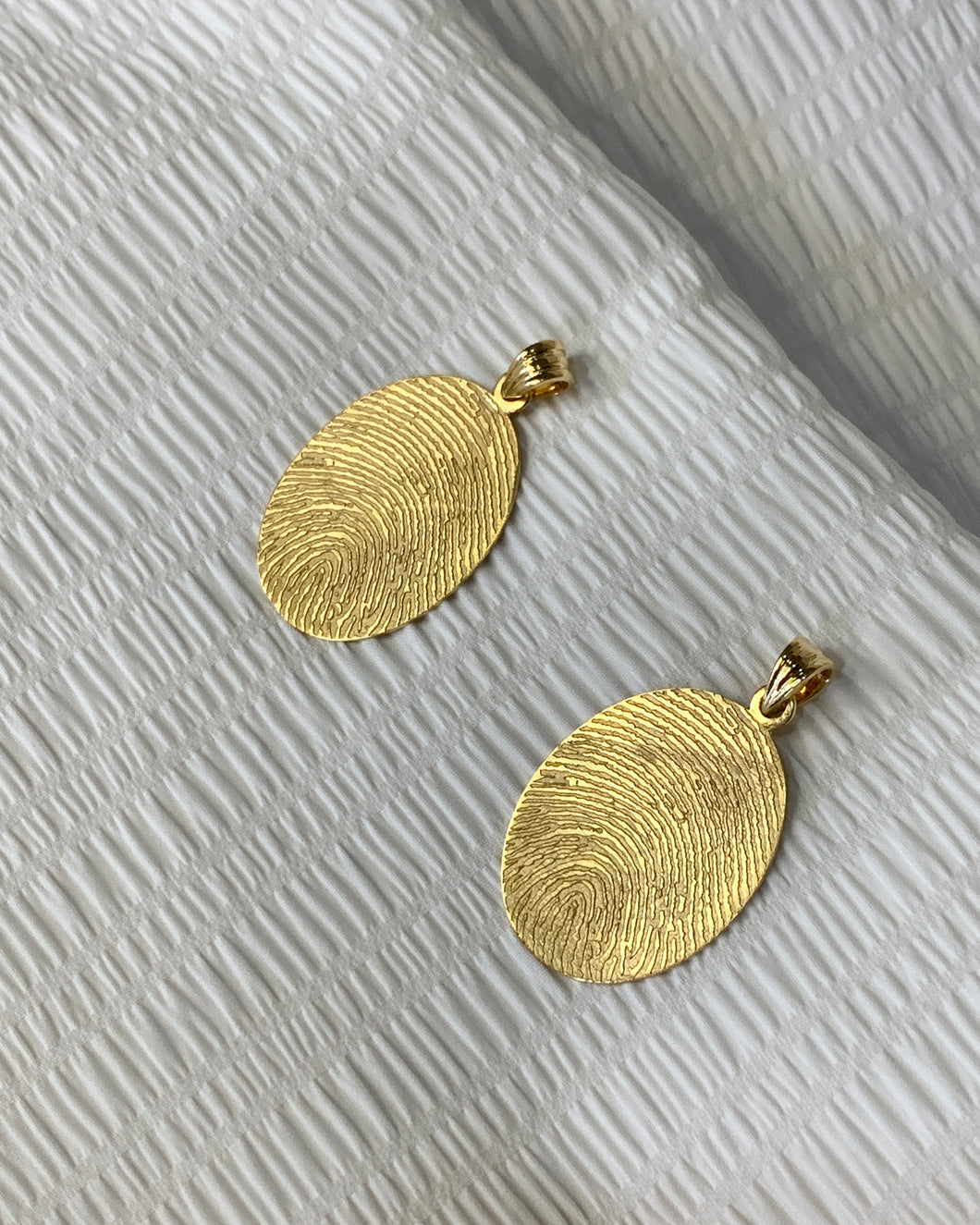 Gold oval fingerprint pendant with engraving of signature at the back.