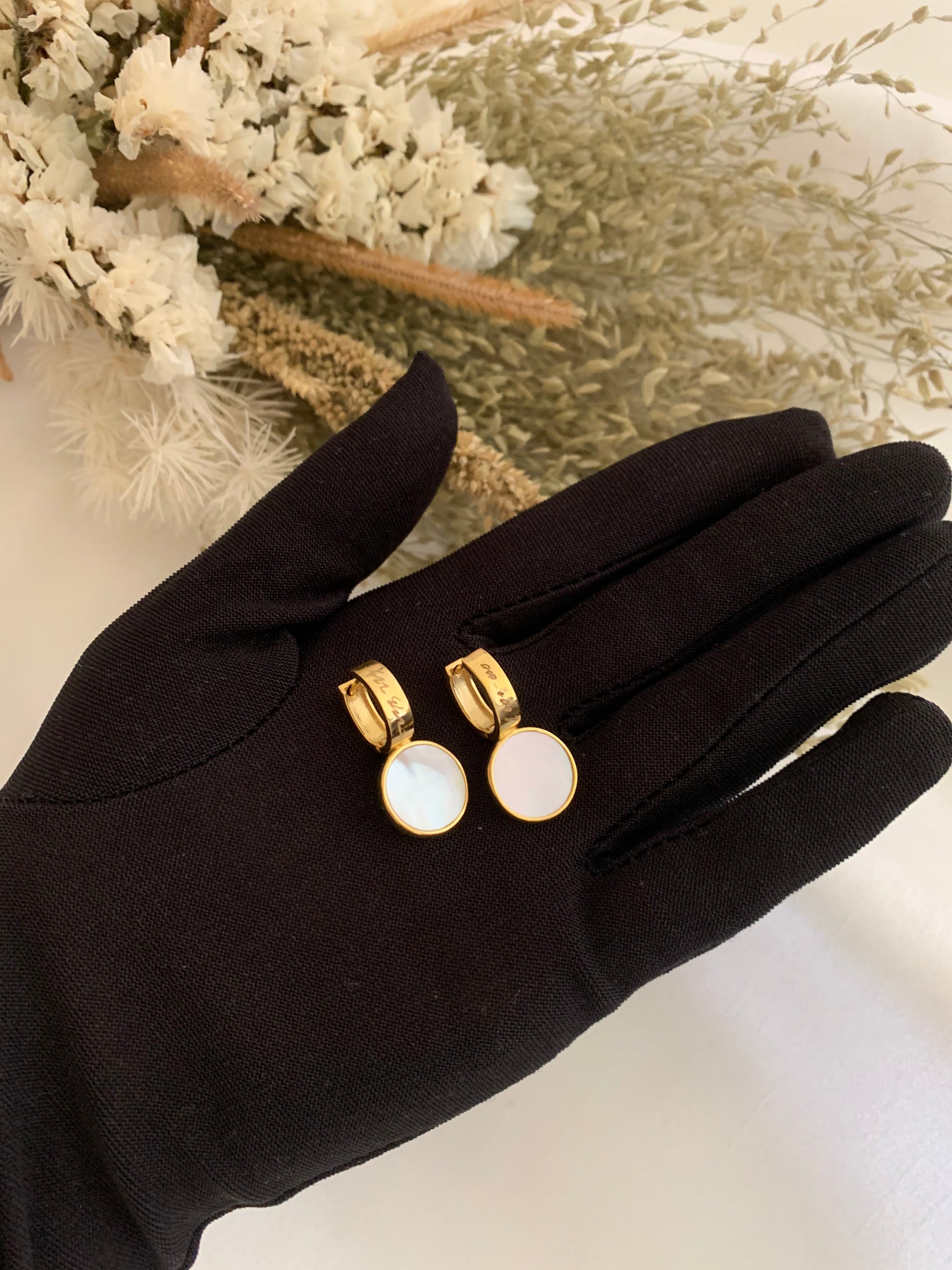 A pair of earrings with a mother of pearl as its main surface then set in 18K yellow gold. The earrings is in a round shaped. At the back of the earrings there is a design in a cross-shaped.