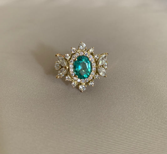 An oval paraiba tourmaline with marquise and round stones around it. Set in yellow gold.