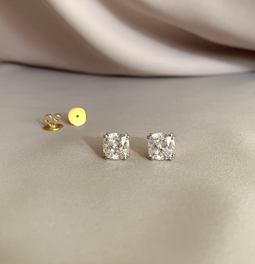Cushion cut diamond studs in 4-prong guarded sets in yellow gold.