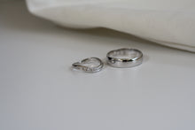 Load image into Gallery viewer, 2 wedding bands in white gold detting. For the husband, its the classic white gold ring. For the wife, its in a slant curve design with small diamonds in it.
