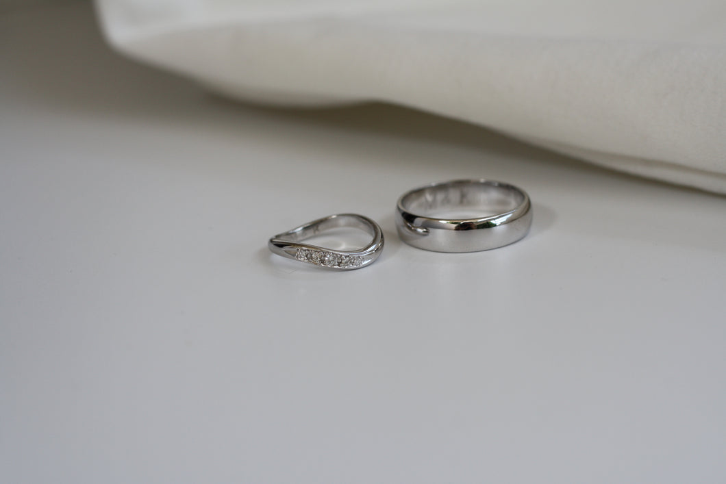 2 wedding bands in white gold detting. For the husband, its the classic white gold ring. For the wife, its in a slant curve design with small diamonds in it.