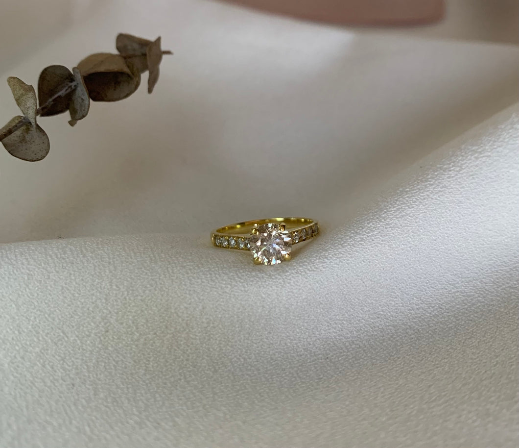 A round diamond enclosed in a 4-claw prong with small sparkling diamonds ,half of the ring. Set in yellow gold.