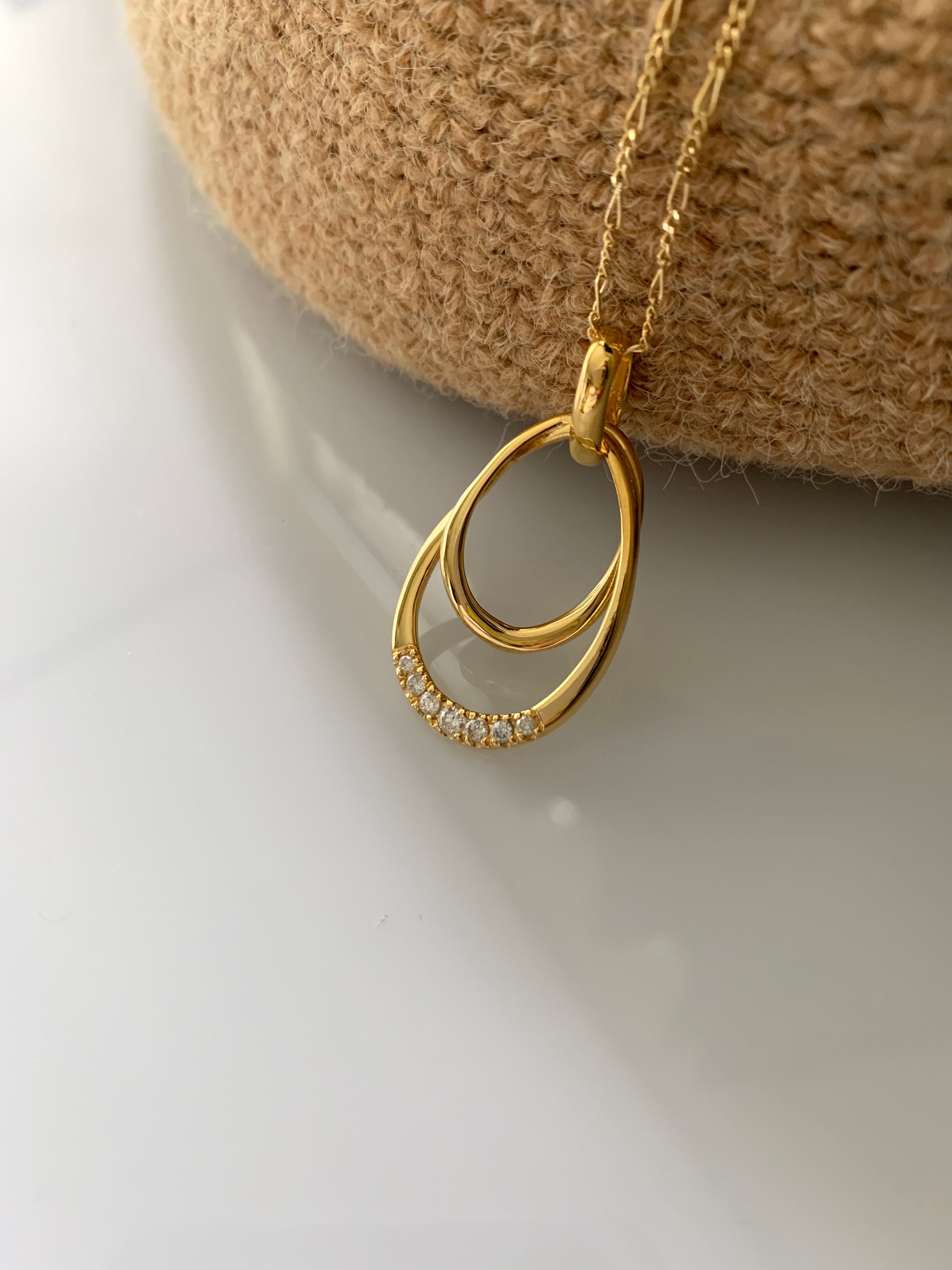 Two intertwined gold oval pendants. With a diamond accent at the center.