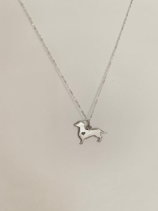 A white gold dog pendant with a heart-shaped stone. 