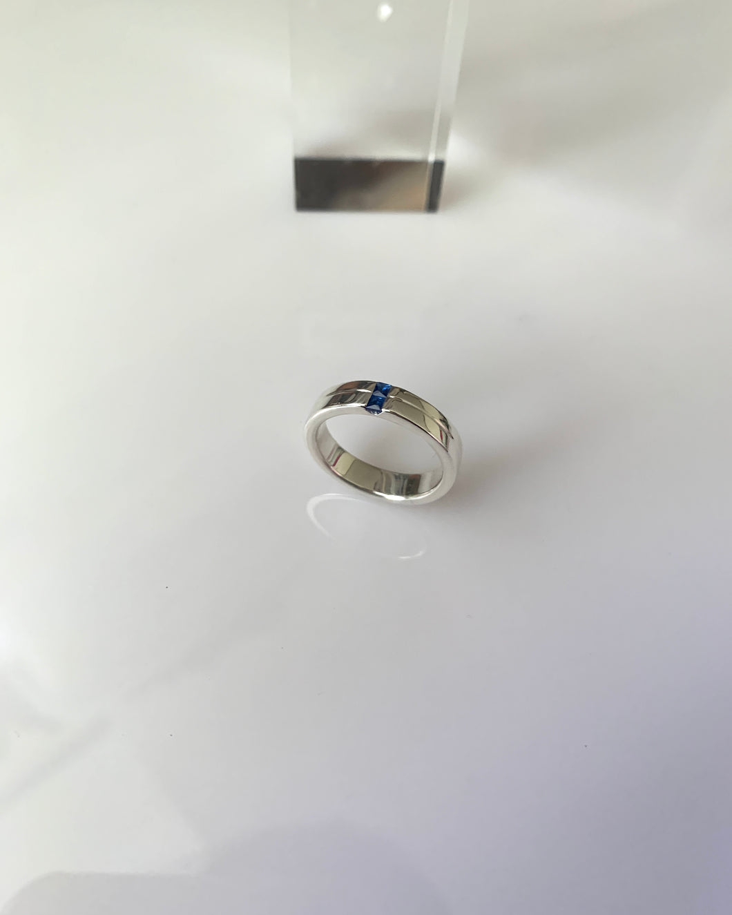 A white gold single band with a textured line at the middle of its thickness. And 2mm princess cut blue sapphires as its center stones.