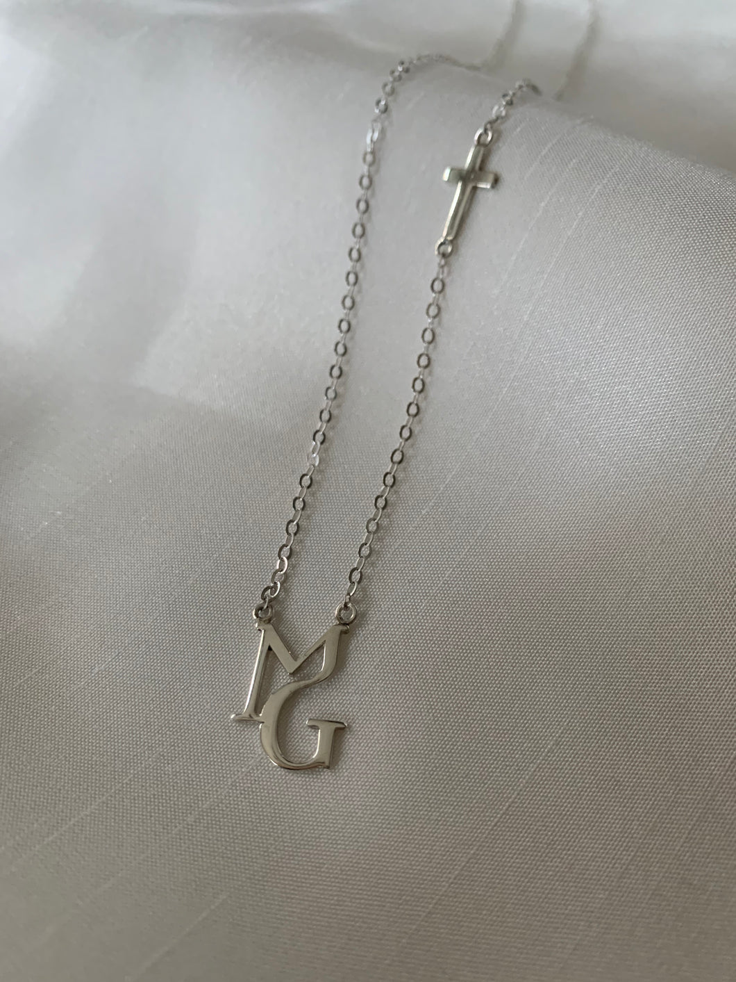 With M and G initials in a unique font with a cross at the aide of the chain. White gold.