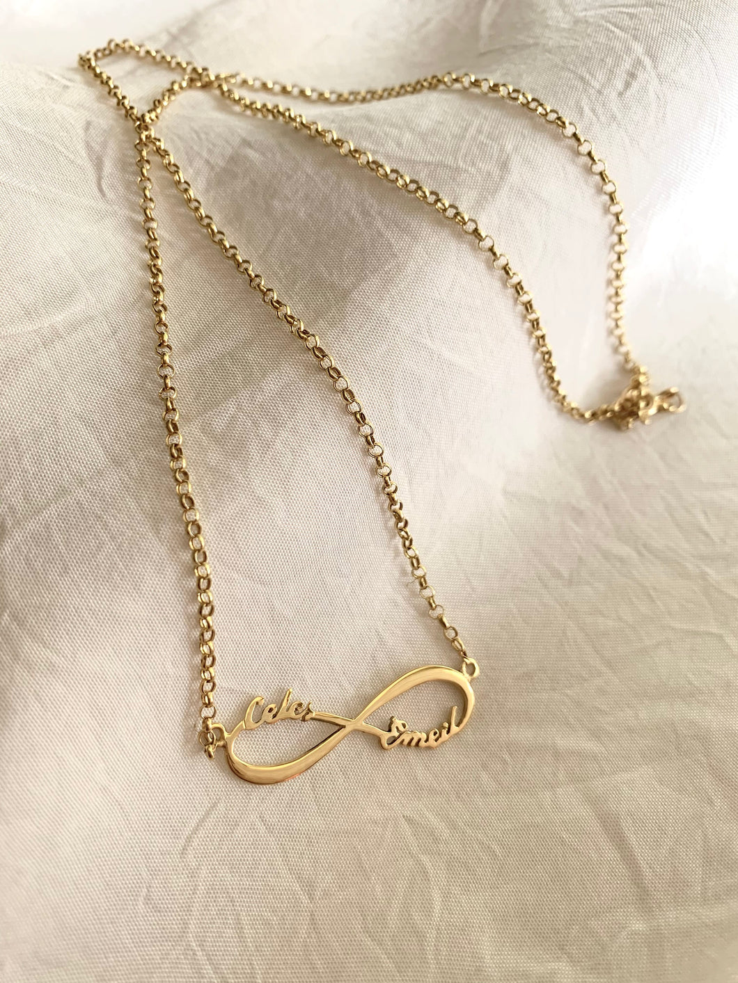 a yellow gold name infinity necklace with two cursive names in it.