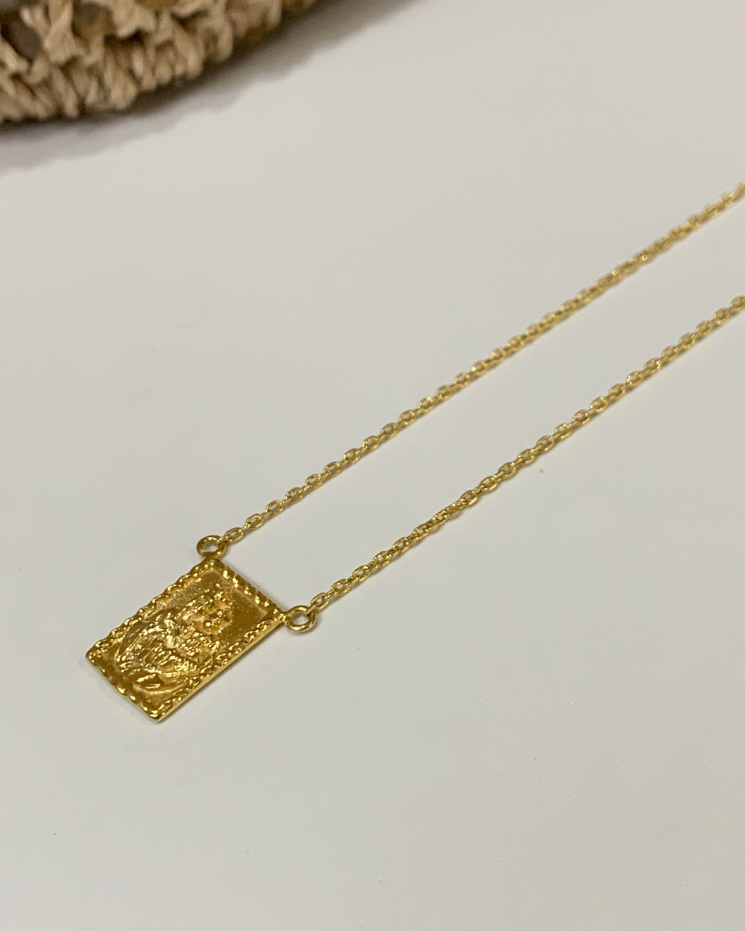 A gold rectangular scapular on a gold cable chain.