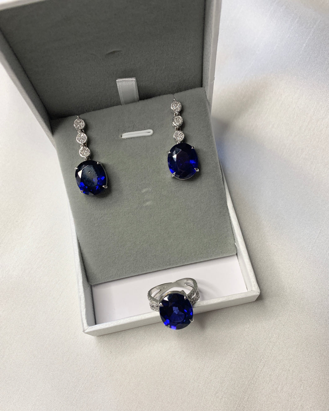 A pair of blue oval sapphires as earrings with 3 round diamonds that makes it into dangling earrings. Paired with an oval blue sapphire ring set in white gold too.