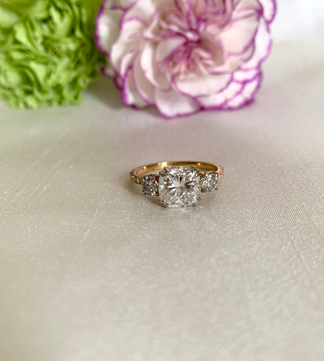 Cushion diamond ring with 2 round diamonds at the side and an additional of 6 small stones on each side too. Set in 18k yellow gold.
