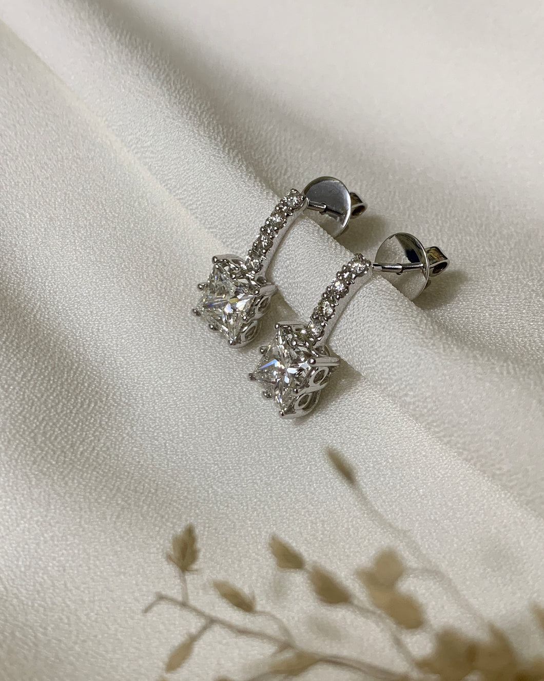 18K white gold princess cut diamond drop earrings with a vertical line of round brilliant diamonds. 