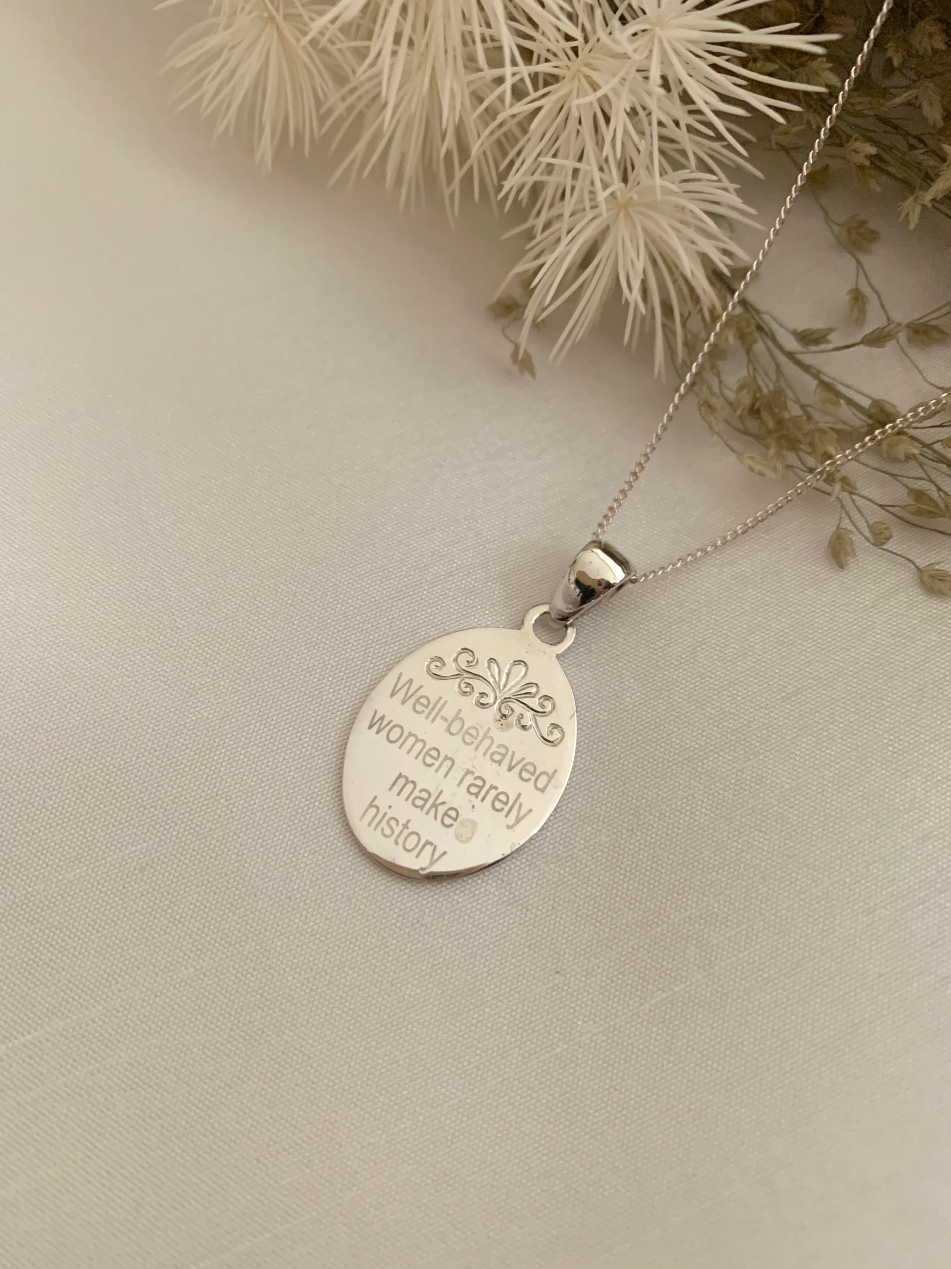 An oval necklace with a saying "Well-behave women rarely make history". 