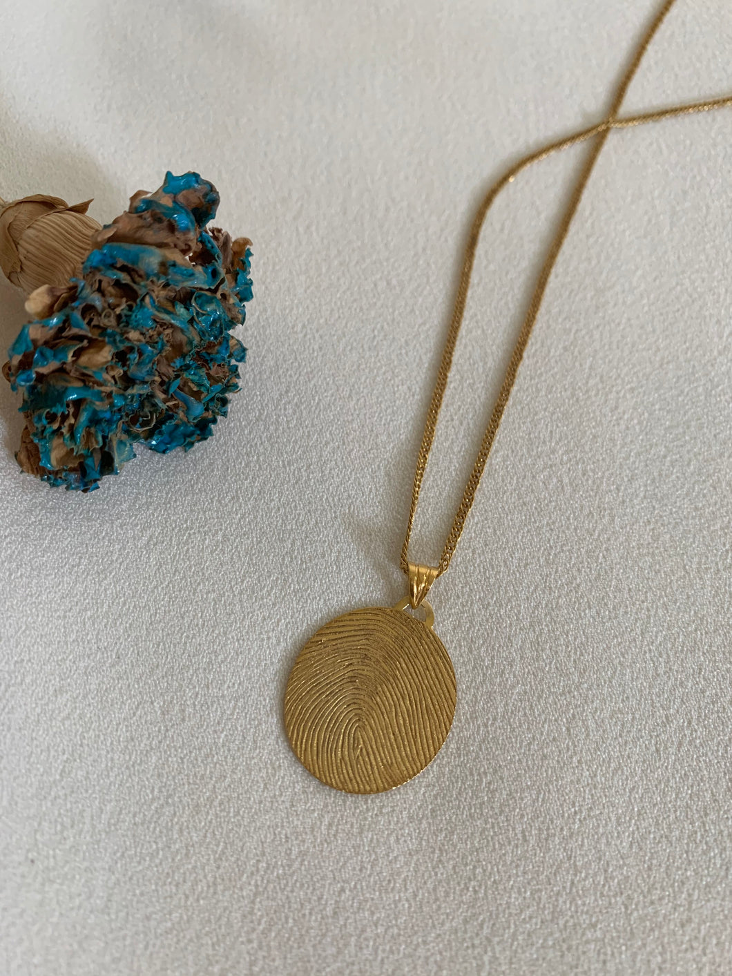 An oval thumbmark necklace in yellow gold.